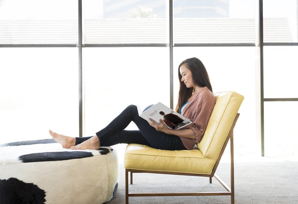mulher lendo revista sentada na poltrona e com as pernas esticadas em um puff