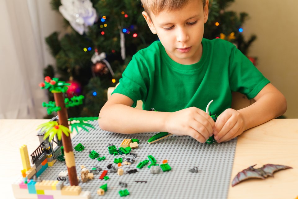 criança sentada em uma mesa com blusa verde brincando com legos