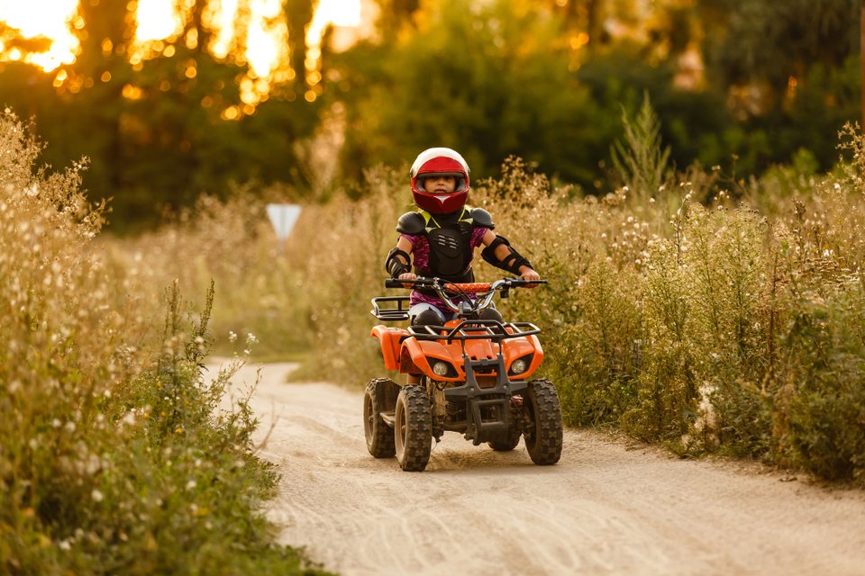 criança de capacete andando de quadriciclo com mato em volta