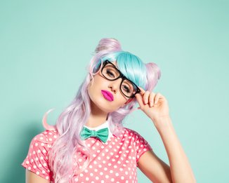 mulher com cabelo rosa e azul, óculos, blusa com bolinhas e gravata borboleta