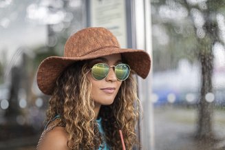 mulher com cabelo cacheado na altura do ombro, chapéu e óculos de sol