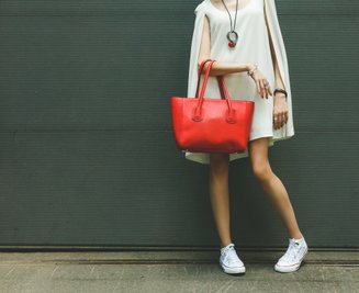 mulher com vestido branco acima do joelho, colar na altura do peito, bolsa vermelha e tênis branco