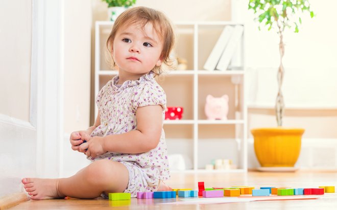 bebê sentado no chão brincando com pecinhas coloridas