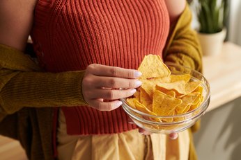 mãos de uma mulher segurando um pote de vidro cheio de doritos