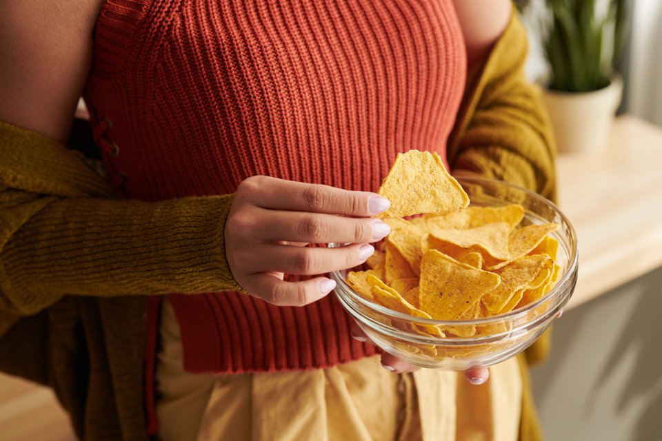 mãos de uma mulher segurando um pote de vidro cheio de doritos