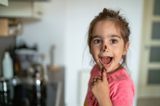 criança com a mão e o nariz sujo de chocolate