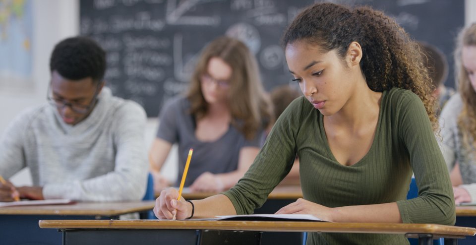 mulher em escola sentada e apoiada na carteira com um lápis na mão escrevendo em um caderno
