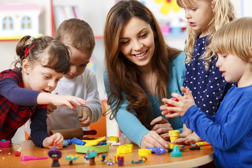 uma mulher e quatro crianças brincando em uma mesa cheia de brinquedos