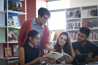 quatro adultos em uma biblioteca olhando pra um mesmo livro