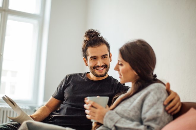 homem e mulher sentados no sofá, ela com caneca na mão e ele com livro