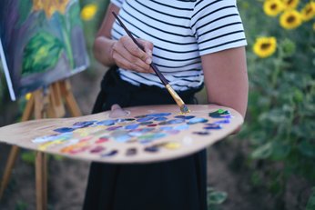 mulher com paleta de pintura cheia de tintas nas mãos