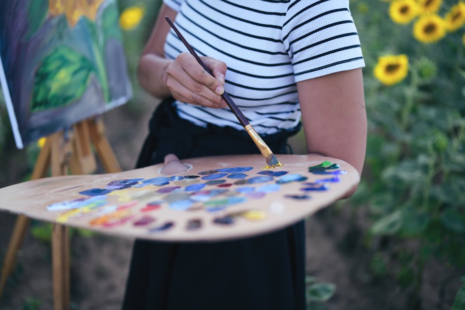 mulher com paleta de pintura cheia de tintas nas mãos