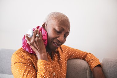 mulher negra com cabelo raspado segurando uma bolsa de gelo na altura do pescoço