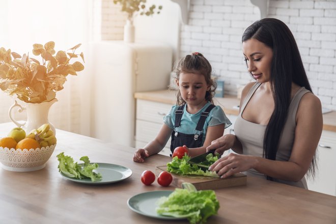 adulto e criança em frente a uma mesa manuseando alface e tomates