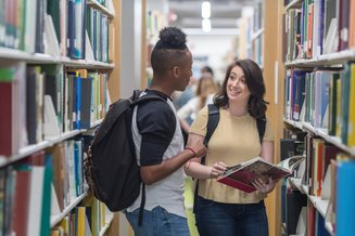 dois adultos conversando em meio a estantes de livros