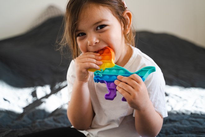 criança com mordedor sensorial em formato de dinossauro na boca