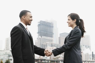 homem e mulher de roupa social dando as mãoes em frente a prédios