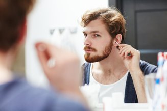 homem usando cotonete no ouvido em frente a espelho