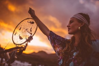 mulher segurando um filtro dos sonhos em frente ao pôr do sol