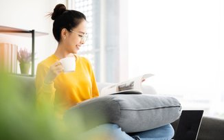 mulher com blusa amarela lendo um livro sentada em um sofá