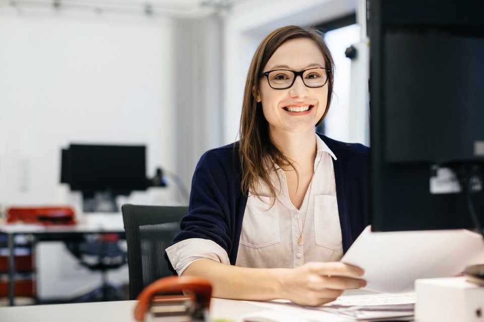 mulher sentada em frente a computador segurando papéis