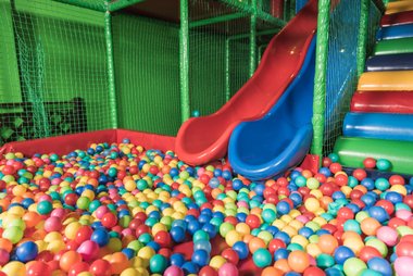 playground com piscina de bolinhas com rede de proteção e dois escorregadores azul e vermelho