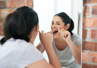 mulher em frente ao espelho usando fio dental nos dentes