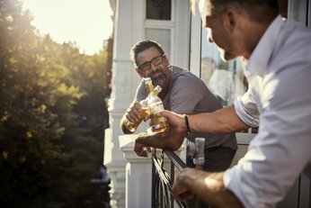 dois homens em uma sacada brindando com garrafas