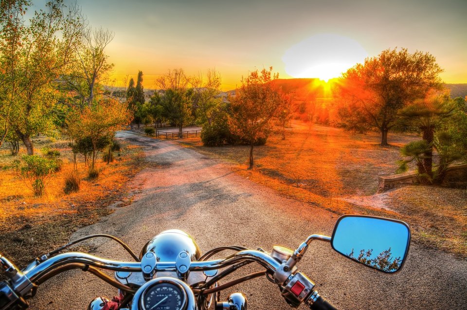 imagem de guidão de moto com vista de estrada de terra e pôr do sol