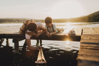 adulto e criança em cima de ponte brincando com um barco no rio