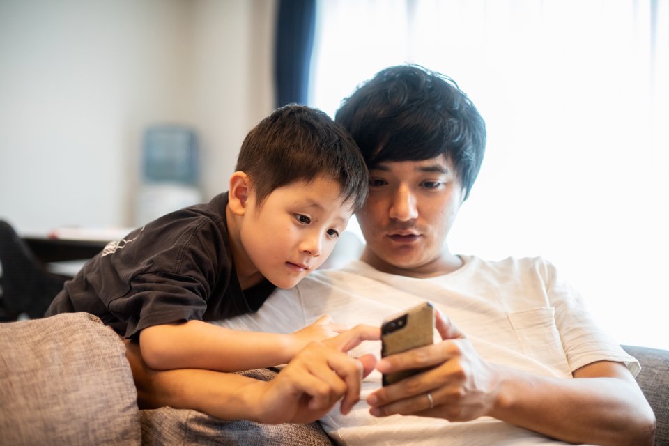 homem e criança no sofá olhando tela de smartphone