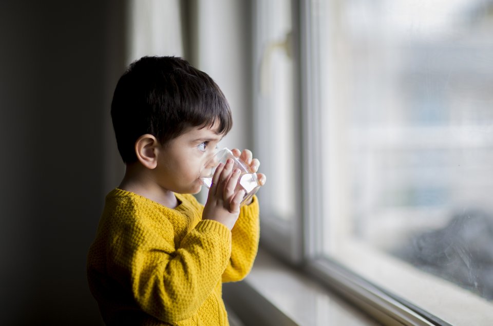 criança bebendo água olhando pela janela
