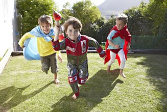 três crianças vestidas de super herói correndo no gramado