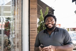 homem negro com celular na mão e camisa polo cinza