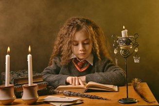 menina com roupa da escola do Harry Potter e cenário com variha, velas, livros