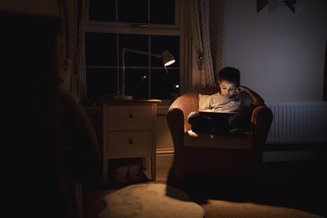 criança em poltrona usando tablet  com ajuda de luz noturna