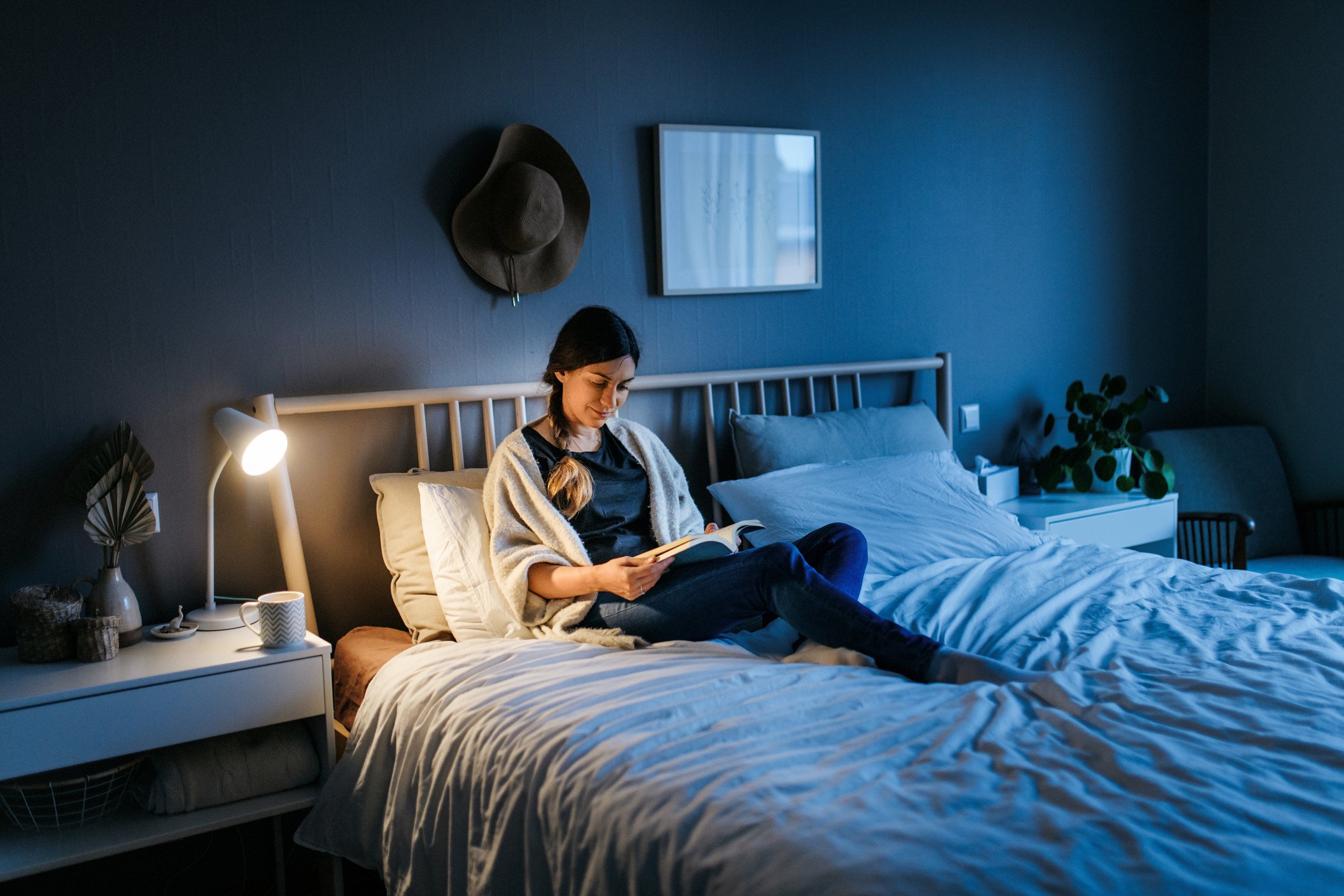 mulher lendo livro na cama com ajuda de luminária
