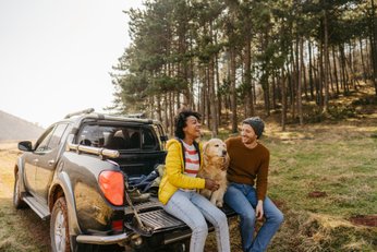 duas pesoas sentadas com um cachorro na traseira de uma pick up