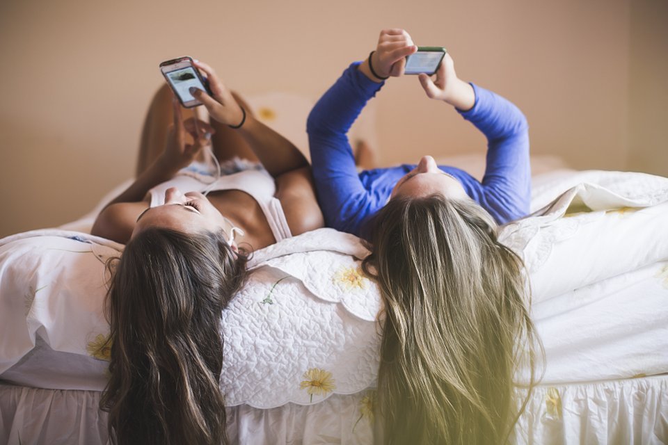 duas meninas mexendo em smartphone deitadas na cama