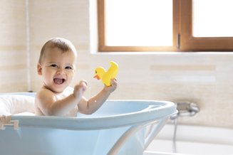 bebê na banheira azul brincando com patinho de borracha amarelo