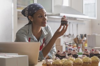 mulher negra com cupcake na mão e vários outros em cima da bancada