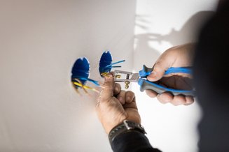 duas mãos segurando um alicate e fios em uma tomada