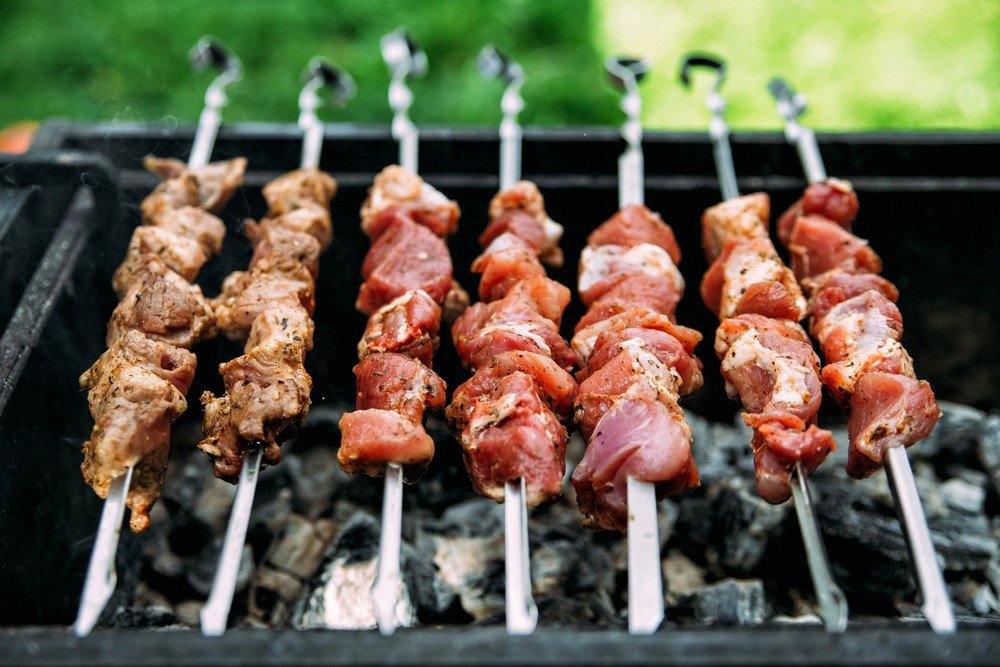 A imagem mostra uma churrasqueira acesa e lotada de espetos de carne para  um suculento churrasco.Tanto o Brasil quanto o…