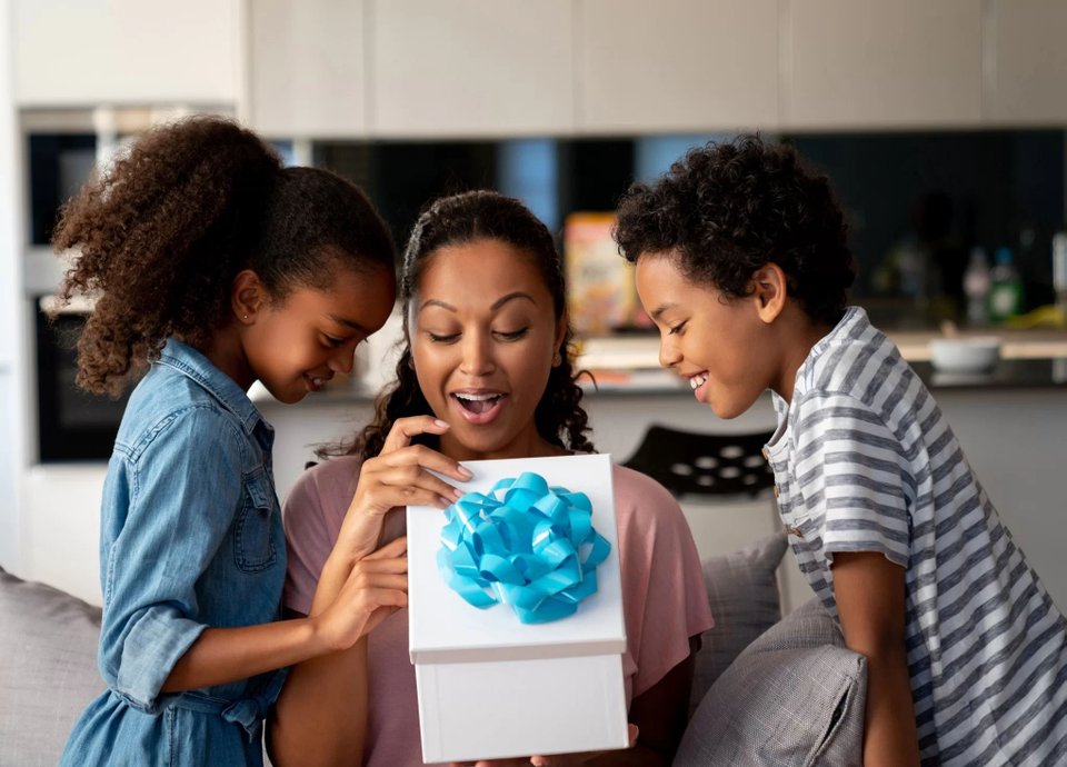 mulher e duas crianças abrindo caixa de presente