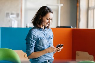 mulher em pé com camisa jeans mexendo em celular