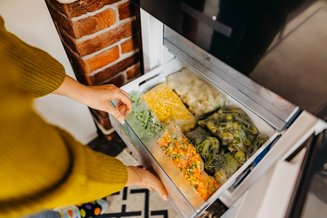 mãos abrindo gaveta da geladeira e ela está com legumes congelados