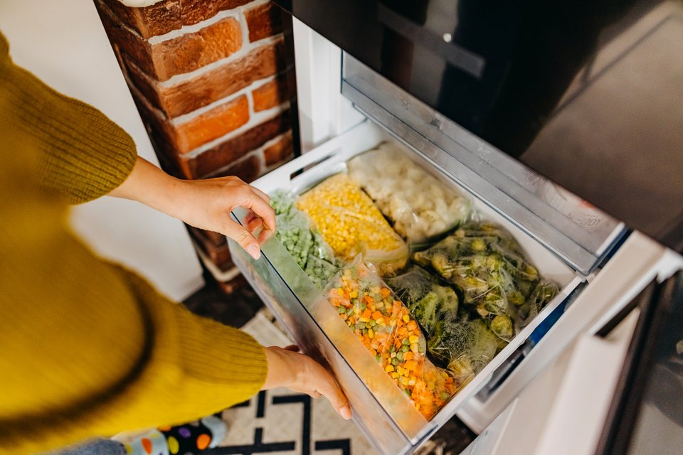 mãos abrindo gaveta da geladeira e ela está com legumes congelados