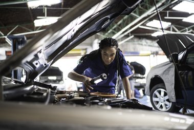 mulher com o capô do carro aberto e uma lanterna na mão