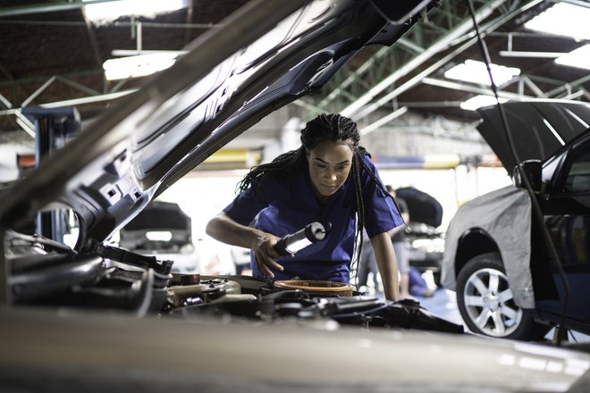 mulher com o capô do carro aberto e uma lanterna na mão