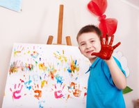 criança com mão com tinta e quadro cheio de mãos coloridas de tinta atrás em cima de um cavalete